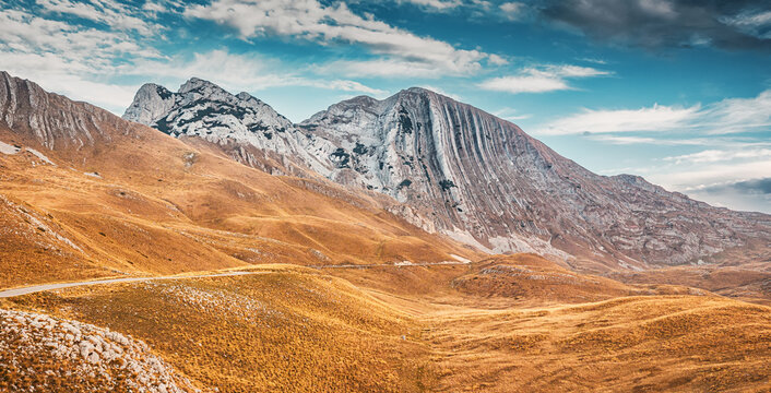 Scenic view of Durmitor national park with a winding road leading towards Bobotov Kuk mountain range under a cloudy sky, travel in Montenegro