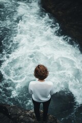 Fototapeta premium Person overlooks turbulent water, rocky cliff edge.