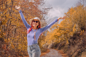 Female hiker with open arms enjoying colorful autumn foliage in a forest path