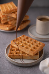 photo A delightful presentation featuring golden-brown waffles being delicately drizzled with rich, melted chocolate, accompanied by a warm cup of aromatic coffee in a cozy setting.