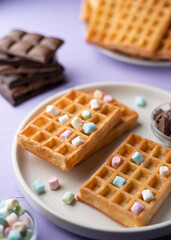 photo Delicious waffles on a stylish plate topped with colorful marshmallows and surrounded by tempting chocolate bars on a pastel background for a perfect breakfast treat