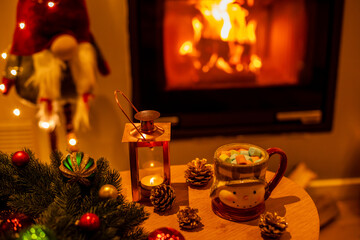 A mug of hot chocolate with marshmallows in wooden table in front of a fireplace as a background.