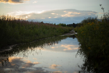 Reflection of clouds in water. Mirror puddle. Reflection of the sky in the river. Evening sky.