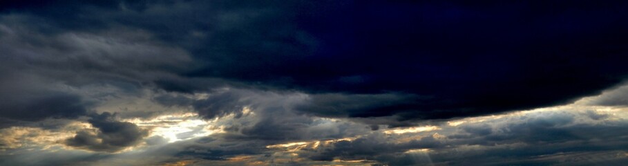Evening dark cloudy sky with sun rays from behind clouds - panorama view, abstract composition with natural pattern of clouds. Topics: weather, rainy, climate, air space, atmosphere, meteorology
