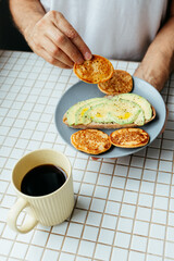 man has breakfast at home in kitchen. plate with avocado toast, pancakes and black coffee. bright and cozy place. healthy eating, vegetarian. top view of food. nutritious lunch, delicious balanced.