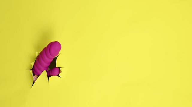 Female hand with magenta vibrator sticking out from yellow paper background. Copy space.