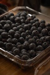 a plastic container filled with fresh blueberries. The container is likely sitting on a wooden surface, given the visible wood grain in the background
