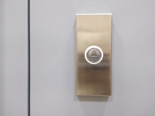 Elevator call button with up arrow on grey wall.