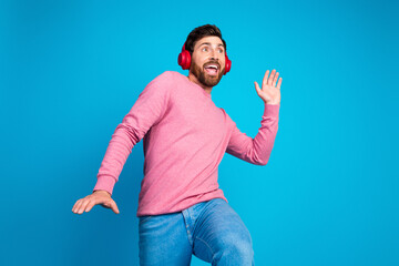 Joyful young man in a pink sweater and red headphones enjoying music against a vibrant blue background