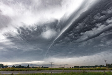Fototapeta premium A large, ominous, low-lying cloud formation hangs over a rural landscape. Stormy weather is imminent.