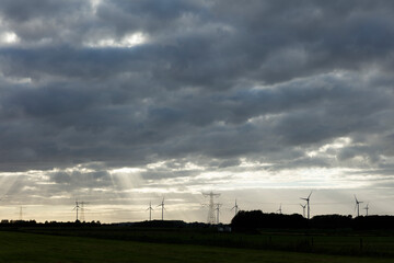 Cloudy sky over a rural landscape with wind turbines and power lines.  Sunbeams pierce the clouds.