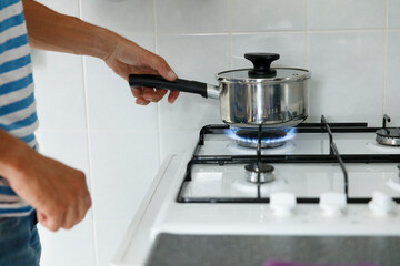Person placing saucepan on lit gas burner.  Cooking in progress.  Kitchen scene.