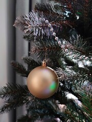 Close-up of a golden Christmas ball ornament hanging on a decorated artificial Christmas tree.