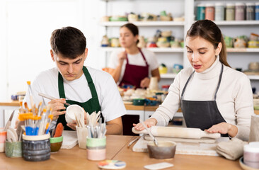 Fototapeta premium Young woman and young man sculpting ceramic product in workshop