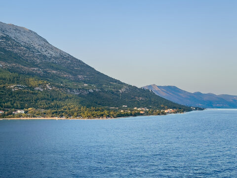 Korcula, Croatia - June 30, 2024: Mainland coastline above Kuciste with tall forested mountain in back. Few buildings along beach