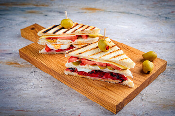 Traditional club toast sandwich with ham, cheese and egg served with vegetables as close-up on a wooden cutting board