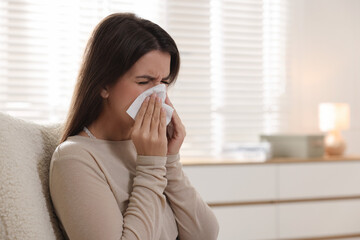Young woman with tissue blowing runny nose at home. Space for text