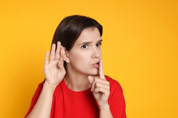 Woman showing hand to ear gesture on orange background