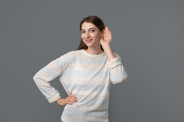 Woman showing hand to ear gesture on grey background