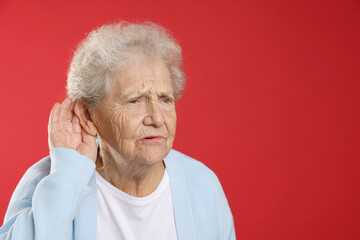 Senior woman showing hand to ear gesture on red background, space for text
