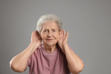 Senior woman showing hand to ear gesture on grey background