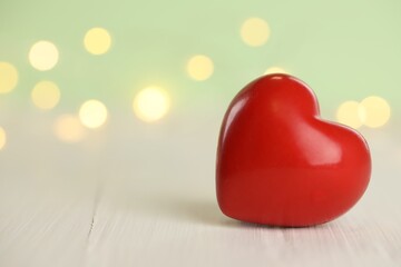 Fototapeta premium Red heart on white wooden table against festive lights, space for text. St. Valentine's day