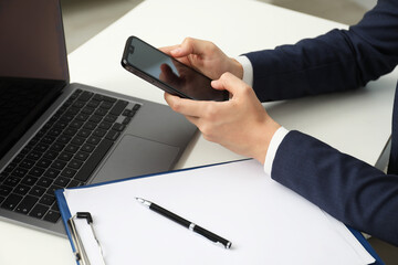 Businesswoman using smartphone at white table indoors, closeup. Modern technology