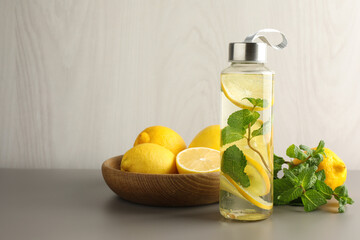 Lemon water with mint in bottle, fresh fruits and leaves on light grey table, space for text