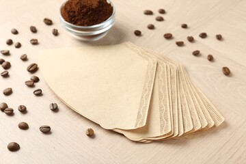 Paper filters, ground coffee and beans on light wooden table