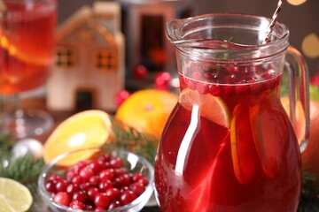 Tasty punch drink in glass jug, ingredients and Christmas decor on table, closeup