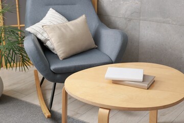 Stylish coffee table with books and rocking chair at home