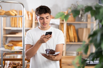 Male customer takes photo of sweet pie using smartphone in interior of a private bakery