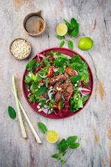 Mixed Thai style green leafy salad with marinated beef and peanuts served with vinaigrette dressing as top view on a design plate