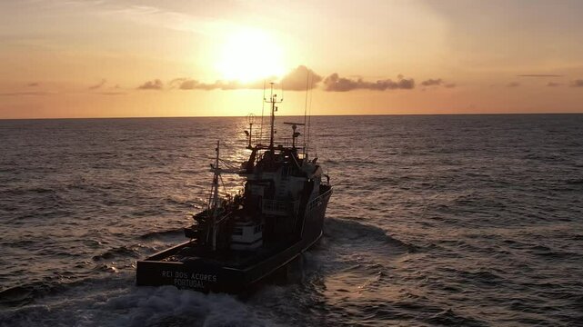 Imagem de um atuneiro navegando nas &aacute;guas do Oceano Atl&acirc;ntico durante o p&ocirc;r do sol, com o barco cortando suavemente as ondas sob a luz dourada e laranja do fim do dia. 