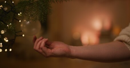 A Woman's Hand Touches a Christmas Bauble Against the Background of a Burning Fireplace