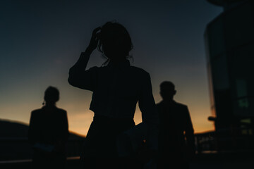 Three silhouetted business people stand outside at sunset, their forms and gestures suggesting professionalism and teamwork. The dramatic lighting adds a sense of mystery and focus to the scene.