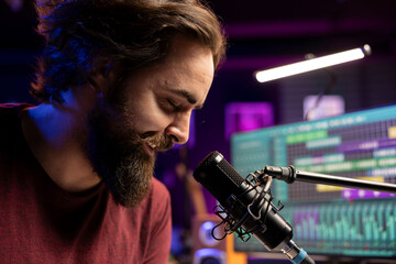 Music composer singing his new lyrics on microphone in home studio, producing soundtracks with daw...