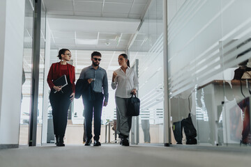 Group of business people confidently walking through a contemporary office hallway, showcasing teamwork and collaboration. They carry documents and bags, representing dynamic work environment.