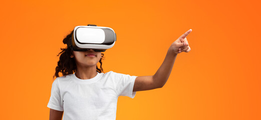 New Futuristic Experience. Black Girl Wearing VR Helmet, Using Virtual Reality Glasses And Pointing Away While Standing Isolated Over Yellow Background In Studio, Exploring Augmented Reality