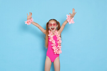 Happy little girl in beachwear and wreaths of flowers on light blue background