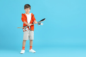 Little boy with skateboard on light blue background, space for text
