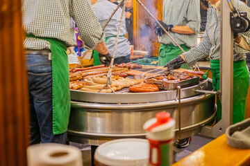 Large sausages grilling on an outdoor barbecue stand with vendors. Concept of traditional market food