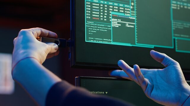 Hacker doing illegal activities in secret underground base, uploading USB flash drive containing data obtained from victim after tricking it into installing ransomware program, camera A