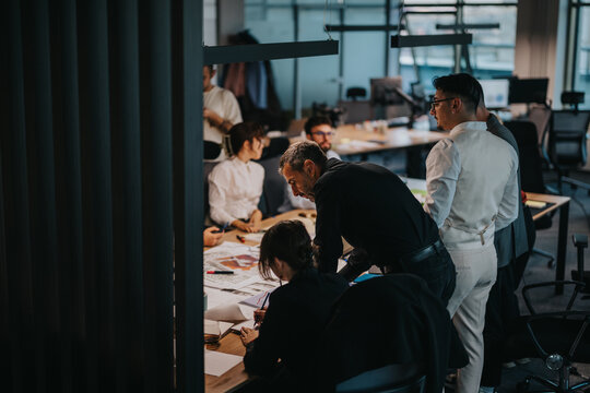 A diverse and multigenerational group of business colleagues collaborate, strategizing and analyzing proposals in an open office environment. The team engages in creative discussions and idea