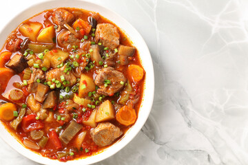 Delicious stew with vegetables in bowl on white marble table, top view. Space for text