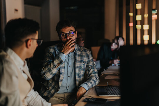 A group of business people engage in a serious conversation while working late at night. The office setting is dimly lit, emphasizing dedication and commitment to their project.