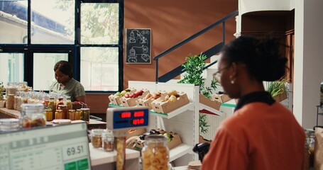 Regular client looking at produce and bulk items in eco store, going grocery shopping to restock organic pantry essentials. African american buyer searching for vegan food choices. Handheld shot.