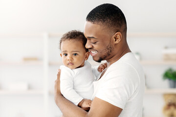 Fototapeta premium Daddy's Love. Happy Black Young Man Embracing His Cute Infant Son At Home, African American Father Holding Adorable Toddler Baby On Arms And Smiling, Enjoying Bonding With His Kid, Copy Space