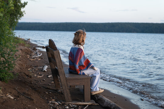 Woman in colorful poncho enjoys serene lake view from bench