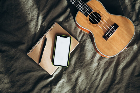 Ukulele, notebook, and smartphone on fabric surface